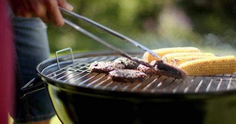 Backyard grilling burgers and corn on charcoal kettle grill with tongs and denim
