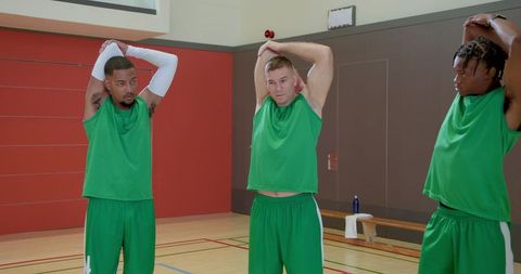 Diverse male basketball teammates stretching overhead in indoor gym warming up for practice