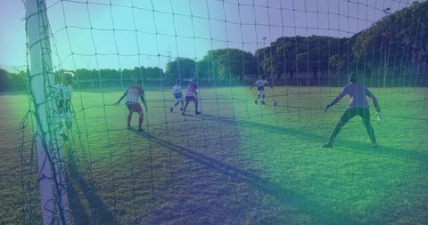 Goalkeeper preparing for shot as attacker charging through defenders on grass soccer pitch