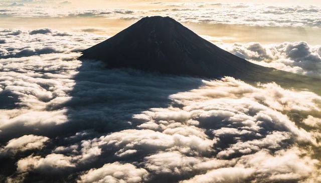Solitary volcanic cone casting triangular shadow over cloud sea at sunrise, aerial vista