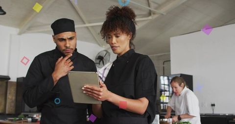 Two chefs collaborating over tablet in industrial kitchen reviewing menu and recipes
