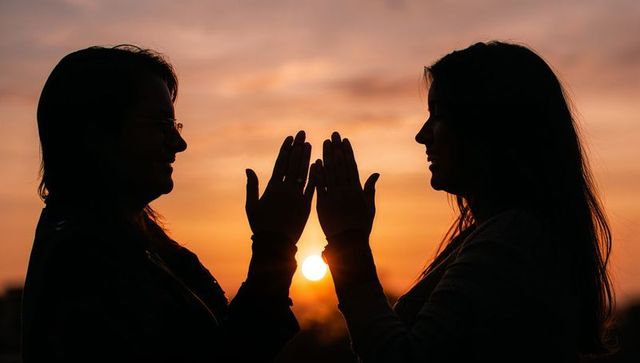 Two women framing sun at sunset silhouette showing friendship and golden hour connection