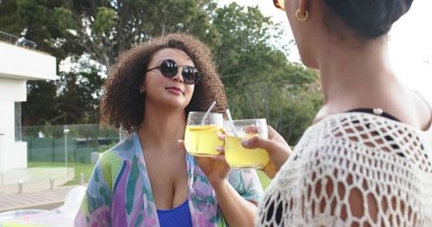 African american friends toasting with cocktails on sunny patio by pool, relaxing together