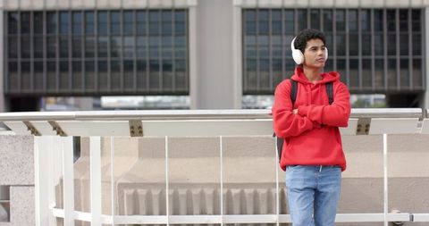 Young man standing on urban walkway wearing red hoodie and headphones looking left