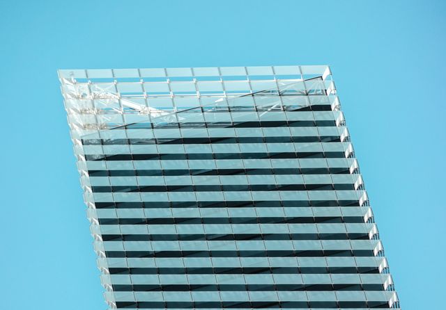 Modern skyscraper with reflective glass surface against clear blue sky. Ideal for concepts related to urban architecture, cityscapes, and modern construction. Useful for marketing materials, business presentations, and real estate promotions featuring advanced and sleek buildings.
