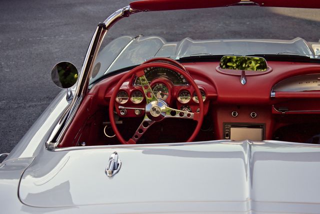 Interior of a classic white convertible car featuring a stylish red dashboard and sophisticated steering wheel detailing. Ideal for use in automotive advertisements, vintage car collections, historic car magazines, luxury vehicle promotions, and classic car event posters.