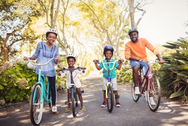 African American family enjoying a bike ride in a park. Parents and children wearing helmets, smiling and bonding while riding bicycles on a sunny day. Ideal for promoting family activities, healthy lifestyles, outdoor fun, and summer leisure.