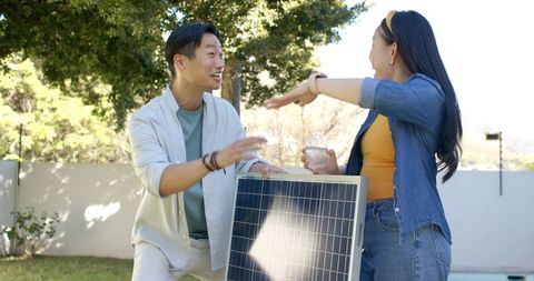 Asian couple discussing solar panel installation in sunny backyard for diy renewable energy