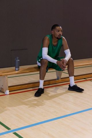 African american basketball player sitting on bench courtside showing focus and hydration