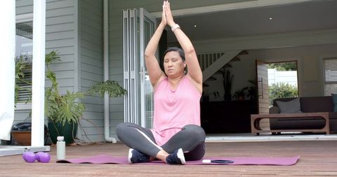 Mature woman meditating on wooden deck practicing yoga for wellness and balance at home