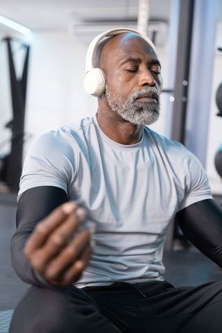 Mature african american man meditating with headphones in gym for mindful fitness