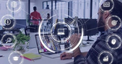 Bearded man working on laptop and smartphone with holographic UI in open office