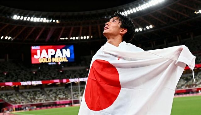 Japanese athlete celebrating olympic gold draping national flag in tokyo stadium night