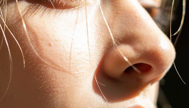 Close-up blonde facial profile showing skin texture, pores and cheek blemish in warm light