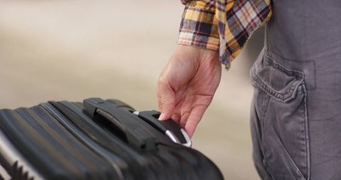 Traveler holding telescopic handle of ridged hard-shell suitcase closeup with plaid shirt