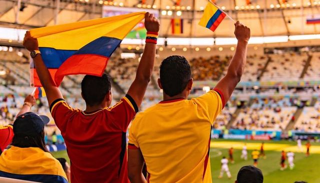 Colombian fans waving flags and cheering at football stadium wearing yellow red jerseys