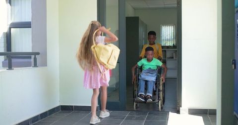 Multicultural students entering school, boy pushing wheelchair, classmate with backpack
