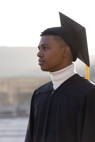 Backlit african american graduate portrait on rooftop in cap and gown with gold tassel