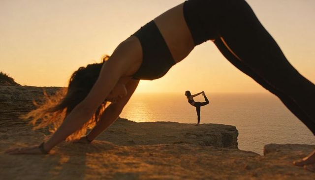 Sunset cliff yoga duo practicing downward dog and dancer pose against ocean horizon