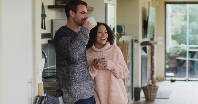 Happy diverse couple talking and drinking coffee in kitchen. spending free time together at home.