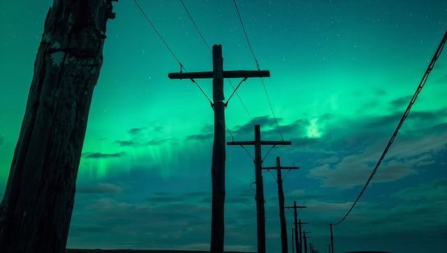 Wooden utility poles leading into vibrant aurora borealis over rural plains at night