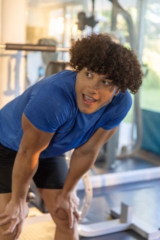 Young man catching breath after intense strength workout at gym bench, blue shirt