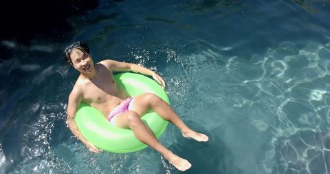 Teenage boy relaxing on green pool float in sunlit water