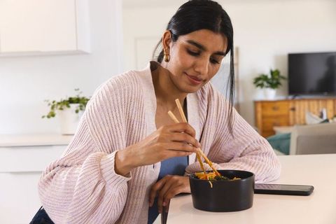 Woman enjoys noodles with chopsticks in cozy kitchen interior