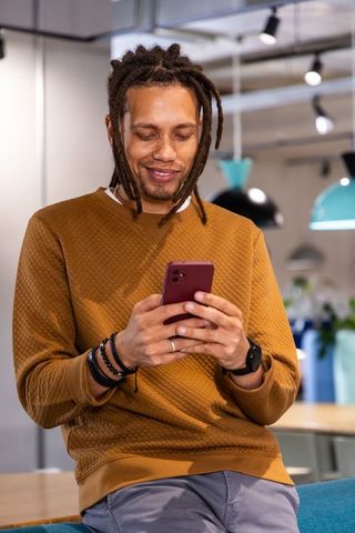African American Man Leaning on Counter Texting in Mustard Sweatshirt at Coworking Space