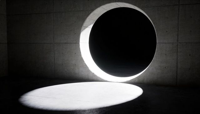Circular aperture casting dramatic spotlight on minimalist concrete chamber floor and wall