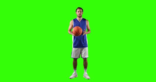 Fully uniformed male basketball player stands holding ball against green screen background. Useful for sports and fitness advertisements, promotional materials, or any visual content requiring a sporty atmosphere. Ideal for use in web design, brochures, articles, or videos about basketball, sports training, or athleticism.