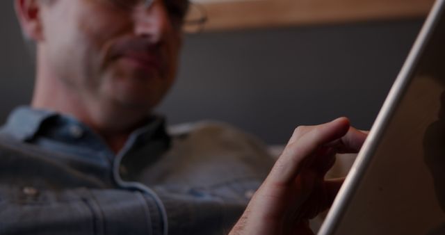 Close-up view of a man using a tablet computer, focusing on his hand touching the screen. The man is dressed casually, providing a relaxed and everyday context. Ideal for illustrating technology use at home, casual browsing, digital interaction, or promoting tablets and related technology. Can be used in technology articles, product promotions, or lifestyle blogs.