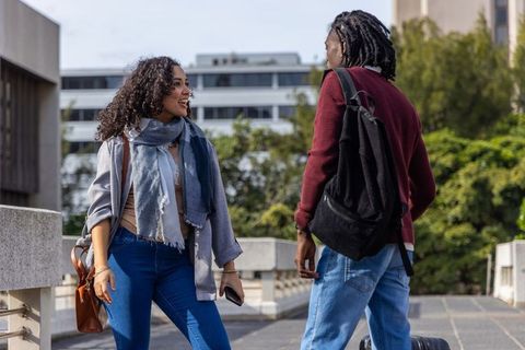 Multiethnic students walking and talking on campus bridge carrying luggage and backpacks