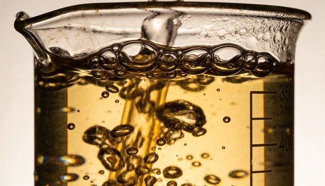 Pouring amber liquid into beaker forming bubbling foam, backlit refraction and flow