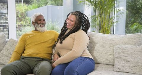 Senior African American couple sharing warm laughter on beige sofa in sunlit living room