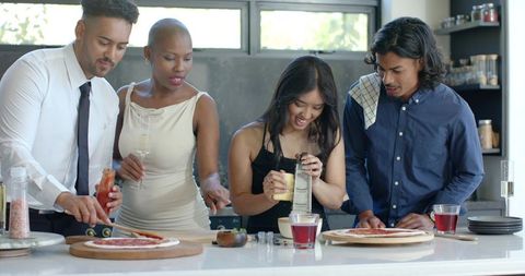 Diverse friends making homemade pizzas in modern kitchen, social cooking party and drinks
