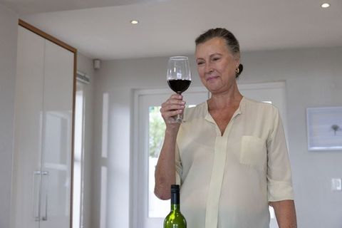 Senior Woman in Modern Kitchen Evaluating Wine in Glass