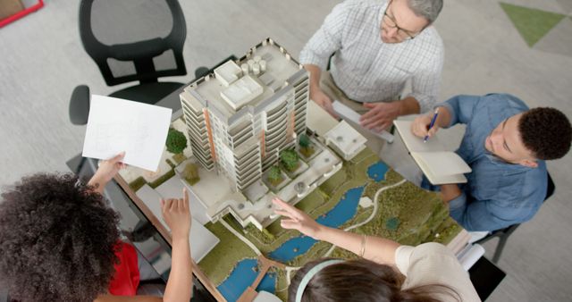 Architects discussing a detailed building model around a table. The photograph showcases professionals collaborating on a construction project. Useful for illustrating team planning sessions, architectural meetings, discussions on blueprints and urban development, as well as professional teamwork in office settings.