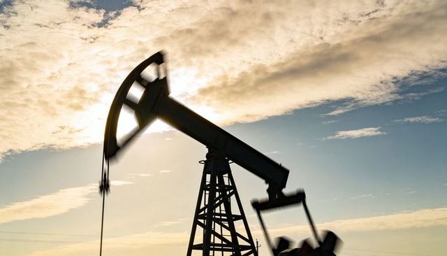 Backlit oil pump jack silhouette sunset over rural plain with dramatic cloudscape