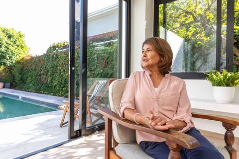 Senior Woman Relaxing by Sliding Glass Doors Overlooking Modern Pool