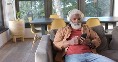 Elderly Man with Headphones Relaxing on Sofa Using Smartphone