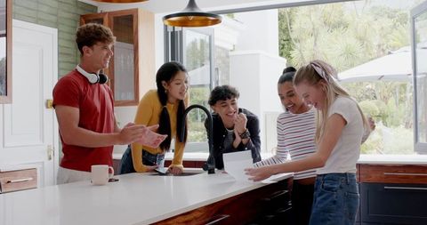 Group of Teens Reading Surprise Note in Modern Kitchen Laughing and Celebrating Together