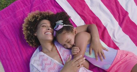 Mother and daughter enjoying summer outdoors bonding on pink towel