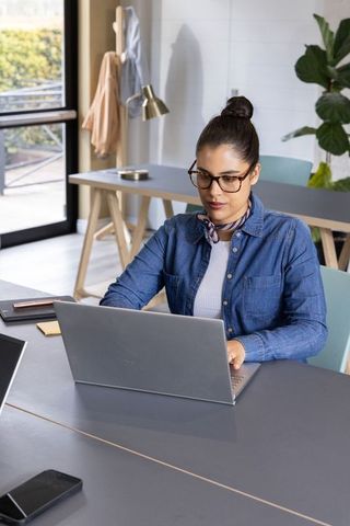 Young professional woman working on laptop in modern coworking space with daylight