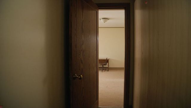 Partly open dark wooden door revealing minimal office interior with desk and chair