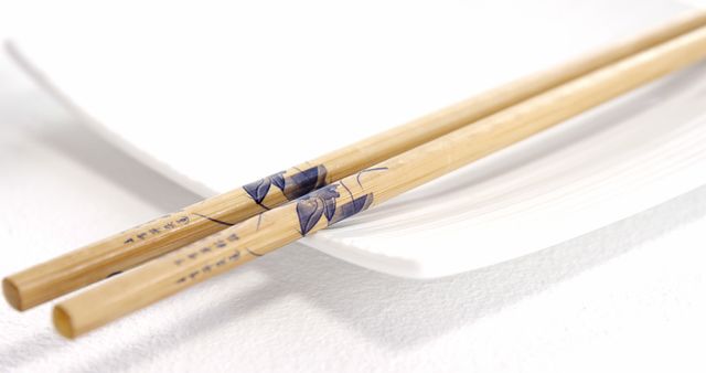 Close-up of traditional wooden chopsticks resting on a white plate, emphasizing simplicity and cultural significance. Useful for topics related to Asian cuisine, cultural traditions, dining etiquette, or restaurant decorations.