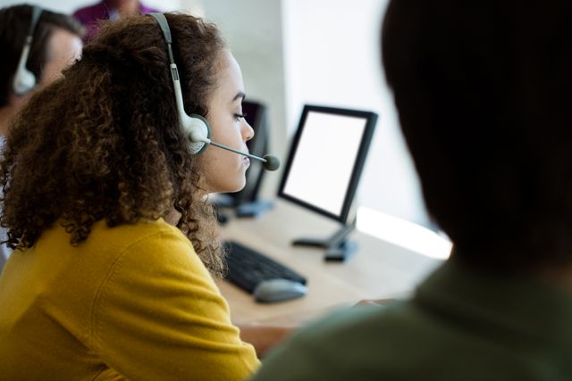 Customer service representative wearing headset working at computer in office. Ideal for illustrating customer support, call center operations, business communication, and professional work environments.