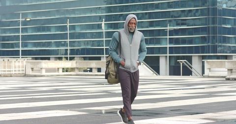 Senior African American man walking across striped urban plaza carrying olive duffel bag