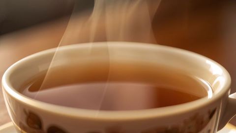 Steaming porcelain teacup with amber tea on wooden counter, floral saucer, cozy morning