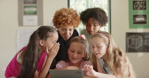 Elementary students leaning around tablet, collaborating and exploring digital learning